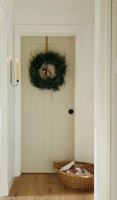 a white door with a wreath hanging on the side of it and a basket in front of it