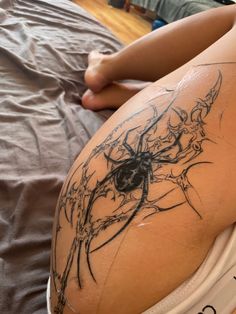 a woman laying on top of a bed with a spider tattoo on her thigh and legs