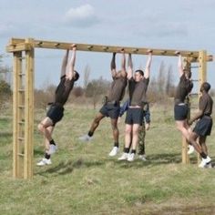 four men are doing exercises on a wooden structure in a field with grass and trees