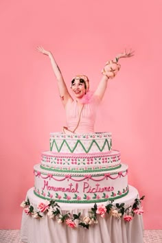 a woman with her arms in the air while standing on top of a large cake