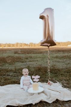 a baby is sitting on a blanket with a cake and balloon in the shape of an 1