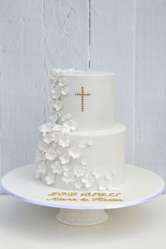 a three tiered cake with white flowers and a cross on the top is sitting on a plate