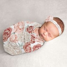 a newborn baby wearing a flowered wrap and headband laying on a white blanket