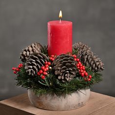 a red candle sitting on top of a metal bowl filled with pine cones and berries