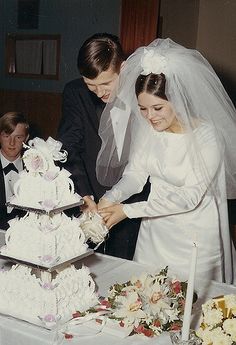 a bride and groom cutting their wedding cake at the table with other people in the background