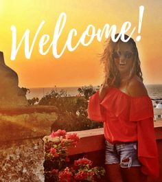 a woman standing on top of a balcony next to the ocean with flowers in front of her