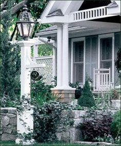 a white house with a clock on it's front porch next to bushes and trees