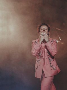 a man in a pink suit standing on stage with his hands clasped to his mouth