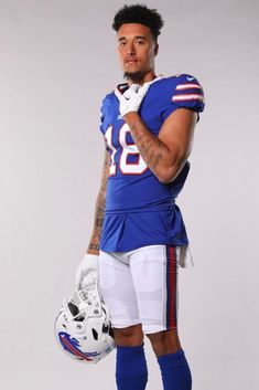 a man in a football uniform is holding a helmet and posing for the camera with his hand on his hip