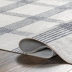 an area rug is laying on the floor with a wooden floor and gray plaid pattern