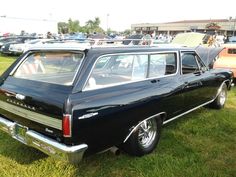 an old black car parked on top of a lush green field next to other cars