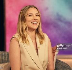 a smiling woman sitting on a couch in front of a colorful background