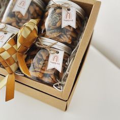 four glass jars filled with cookies in a box next to a gold ribbon and tag