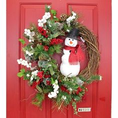 a snowman wreath on a red door with white flowers and greenery around it