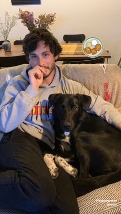 a man sitting on top of a couch with a black dog laying next to him