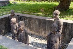 three statues are in the middle of a concrete pit with gravel around them and grass behind them