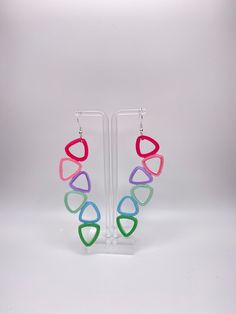 a pair of colorful earrings hanging from a clear display stand on a white background in front of a plain backdrop