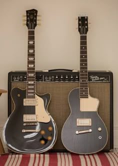 two guitars sitting next to each other in front of an amp and guitar case on a striped rug