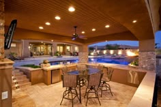 an outdoor kitchen and dining area with pool in the background