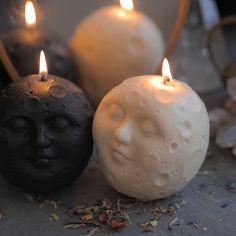 three candles with faces on them sitting next to each other in front of some rocks