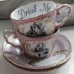 two tea cups and saucers with the words drink me on them, sitting next to each other