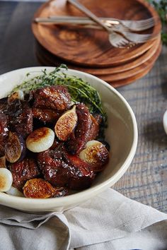 a white bowl filled with meat and vegetables on top of a wooden table next to silverware