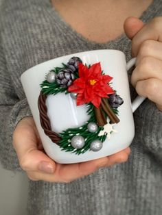 a person holding a coffee mug with a christmas wreath and poinsettis on it