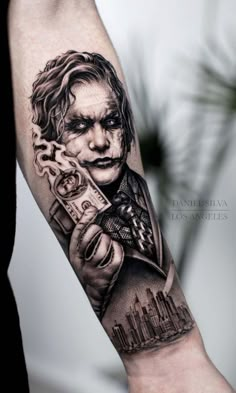 the joker tattoo on the arm is done in black and grey ink, with a city skyline