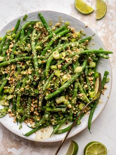 a white plate topped with green beans covered in seasoning next to sliced limes