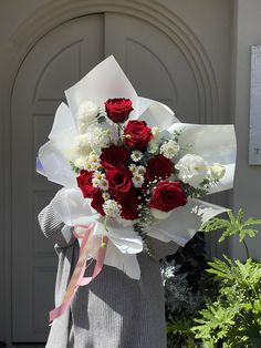 a bouquet of red and white flowers in front of a door with a ribbon around it