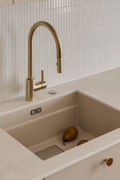 a kitchen sink with a brass faucet and white counter top, next to a beige cabinet