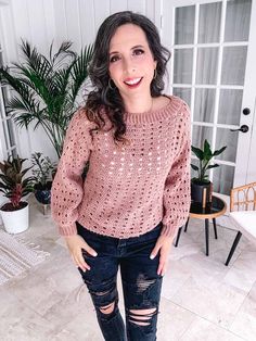 a woman wearing ripped jeans and a pink sweater standing in front of a potted plant