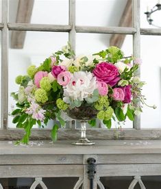 a vase filled with lots of flowers sitting on top of a table next to a window