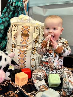 a baby sitting on the floor next to a bag and toy animals with other toys around it