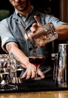 a bartender pouring a glass of red wine into a goblet at a bar