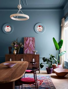 a dining room with blue walls and wooden furniture in the center, potted plants on either side of the table