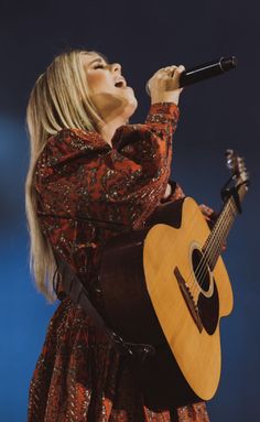 a woman holding a guitar and singing into a microphone