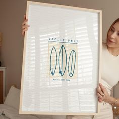 a woman holding up a framed poster with three surfboards on it's sides