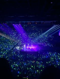 the stage is lit up with purple and green lights as people watch from the stands