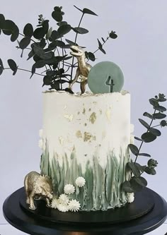 there is a white cake with green decorations on the top and two animals sitting on it