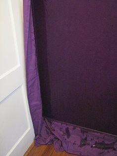 a purple shower curtain in a bathroom next to a white door and wooden flooring