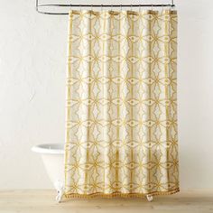 a shower curtain with yellow and white designs on it, in front of a bathtub