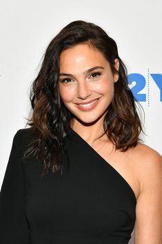 a woman in a black dress smiling at the camera with long hair and shoulder length curls