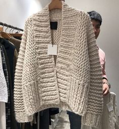 a white sweater hanging on a rack in a clothing store with people looking at it