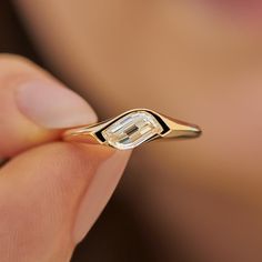 a close up of a person's hand holding a gold ring with an emerald stone