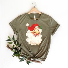 "Cute Santa Face Shirt, Vintage Santa Claus T-Shirt, Christmas Santa Shirt, Christmas T-Shirt, Funny Christmas Tee, Cute Santa Tee, Xmas Tee ☀️☀️☀️☀️☀️ Everything in our shop is hand crafted and made to order. If you want different color or size contact me! If you would like something custom made to fit your personal style please message me and I will do everything to get you that something special. ---How To Order--- ⭐️Please, check and review all photos ⭐️Choose your t-shirt size and color ⭐️Enter your Design Color Example: \"White\" ⭐️Click add to cart. You can go back to add more product ⭐️Click \"Proceed to check out\" ⭐️When you check out, you can add a note to seller for any request *High quality and super soft, comfortable shirt. Made with top of the line vinyl and pressed with a p Funny Print Tops For Christmas Gift, Christmas Crew Neck Shirt Gift, Christmas Graphic Tee Shirt For Holiday, Christmas Gift Crew Neck Shirt, Christmas Graphic Tee Shirt Gift, Christmas Graphic Tee As Gift, Funny Print Tops For Christmas Gifts, Graphic Print Top As Christmas Gift, Christmas Cotton T-shirt Gift