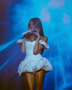 a woman standing in front of a blue background holding her hands up to her face