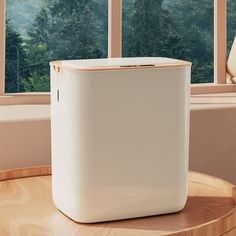 a white cooler sitting on top of a wooden table next to a window with trees outside