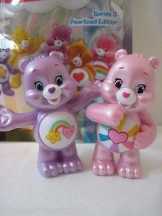 two toy bears are standing next to each other on a table with the package behind them