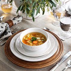 a white bowl filled with soup sitting on top of a wooden place mat next to silverware